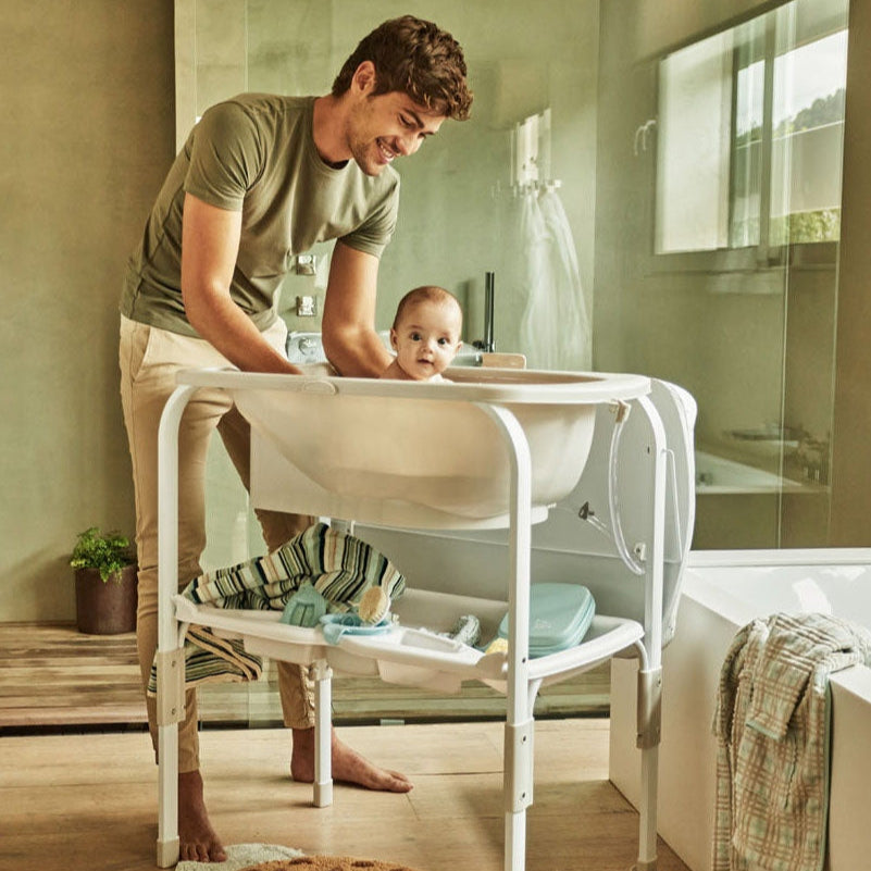 Man bathing a baby in a portable bathtub in a bathroom.