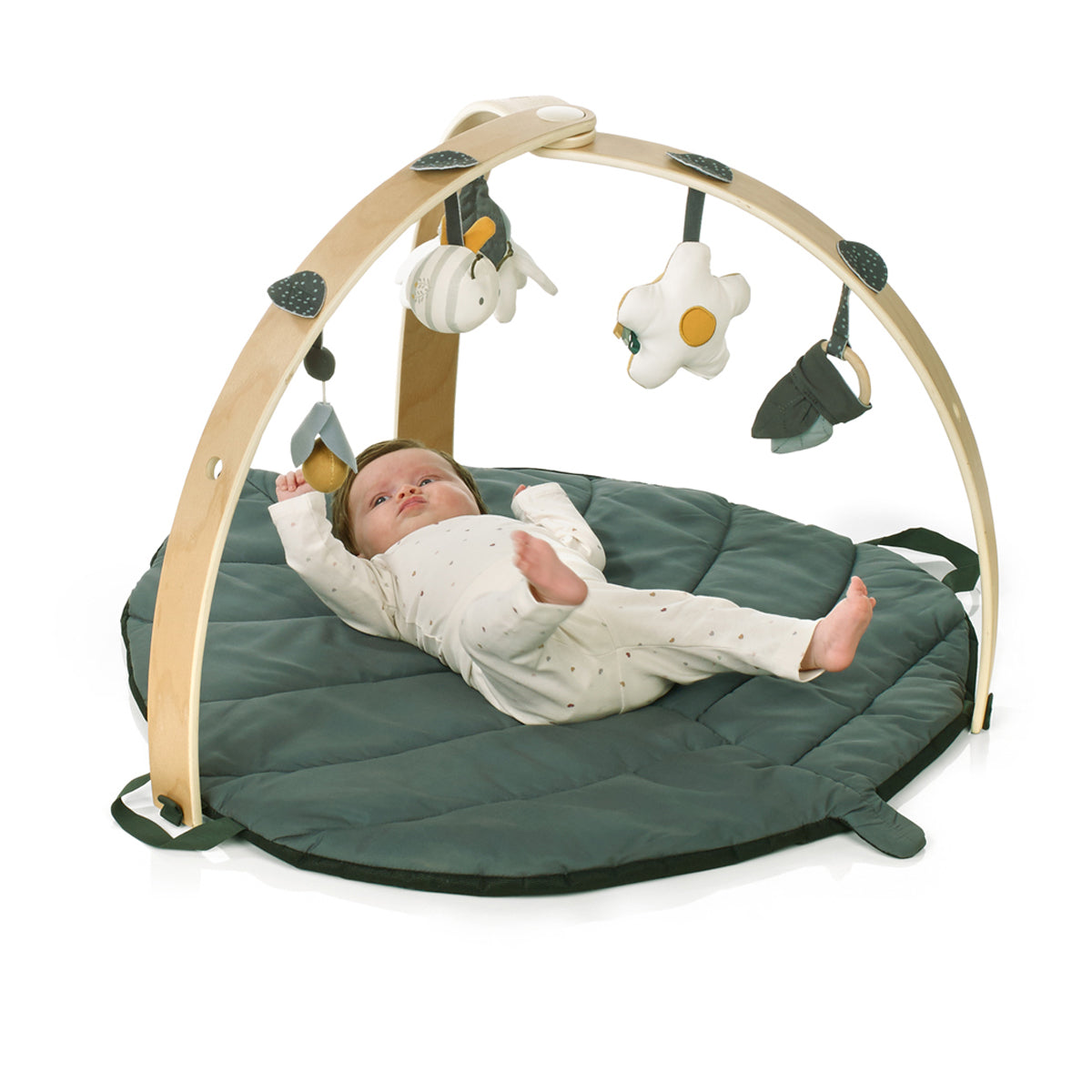 Baby lying on a green play mat with a wooden arch and hanging toys on a white background