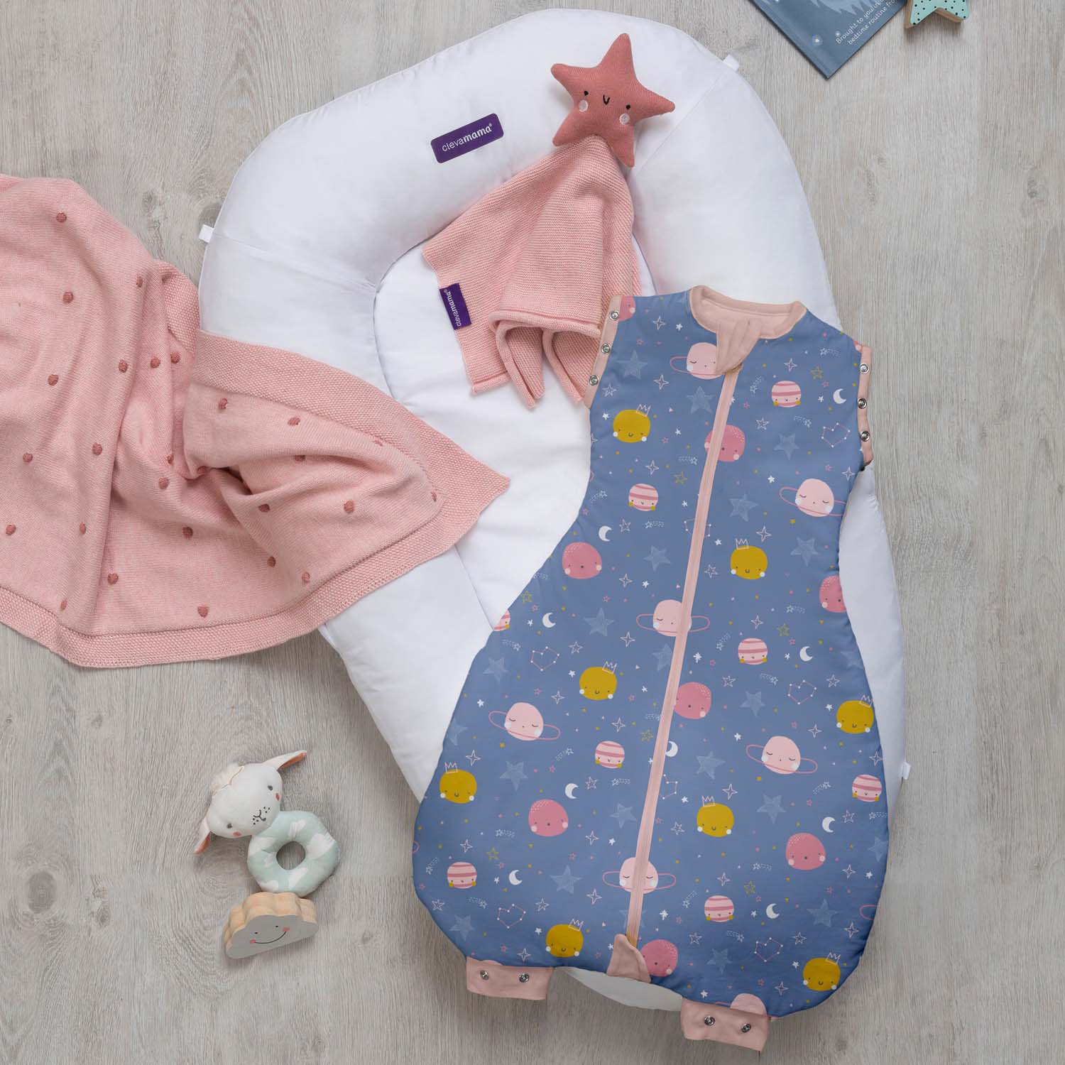 Baby boppy with pink blanket and blue patterned bag on a wooden floor
