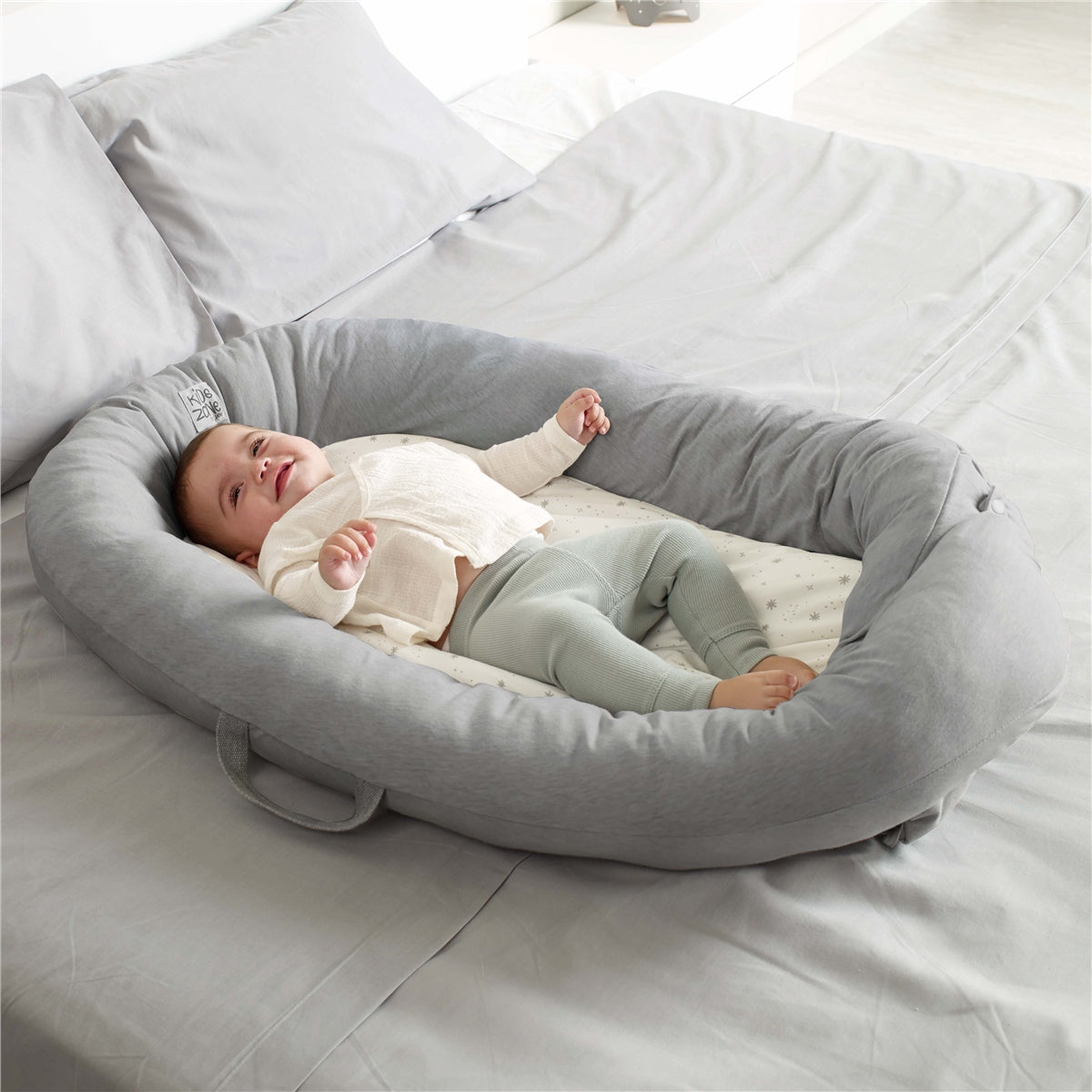 Baby lying in a gray baby bed on a bed