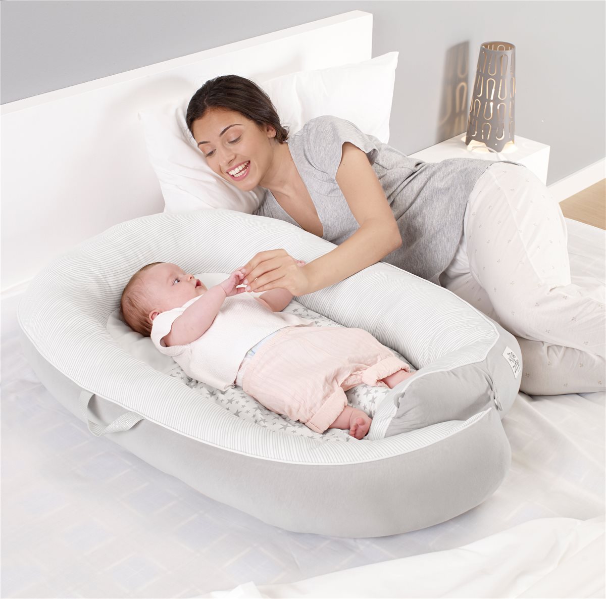 Woman lying on a bed with a baby in a white bassinet.