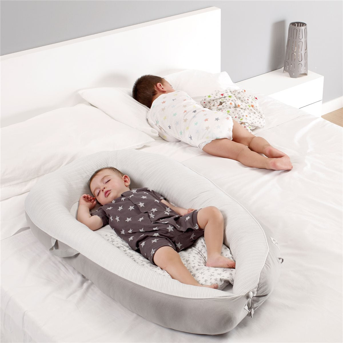 Two children sleeping in a white crib with a gray bumper.