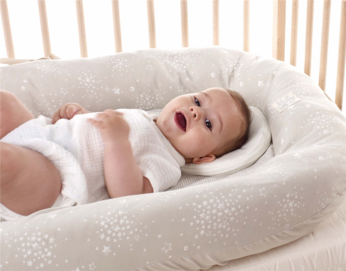 Baby lying on a white cushion with star patterns in a crib.