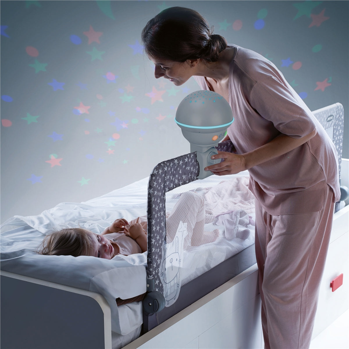 Woman holding a baby monitor over a child in bed with colorful star decals on the wall.