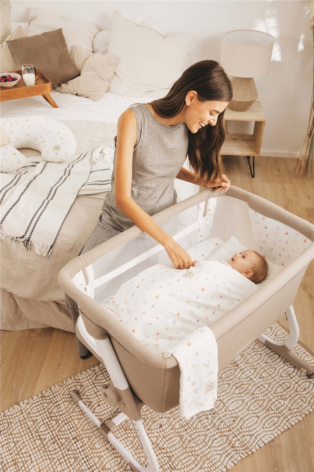 Woman placing a baby in a portable crib in a bedroom setting