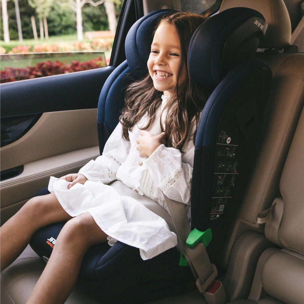 Child in a car seat with a garden visible through the car window