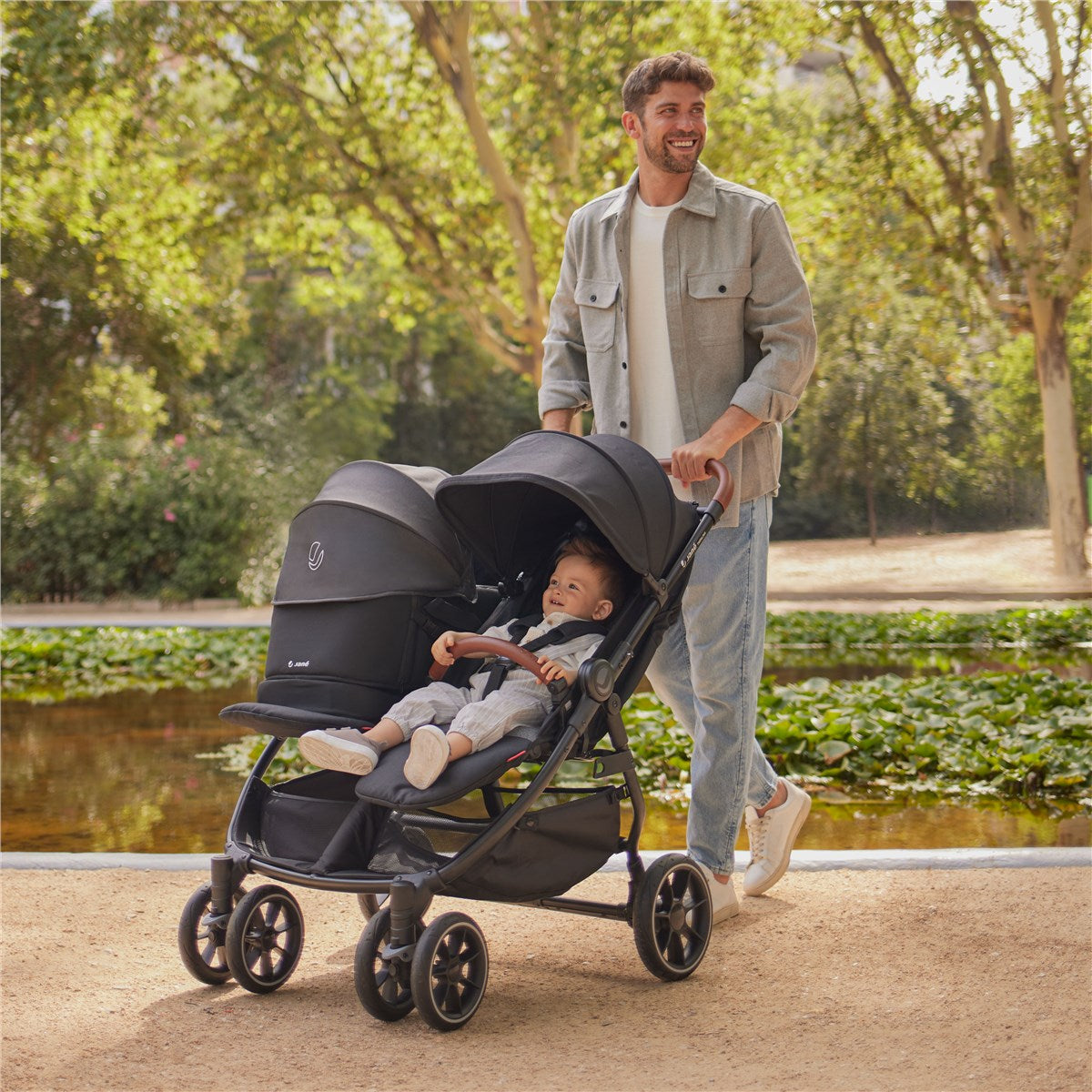 Man pushing a double stroller with a child in a park setting