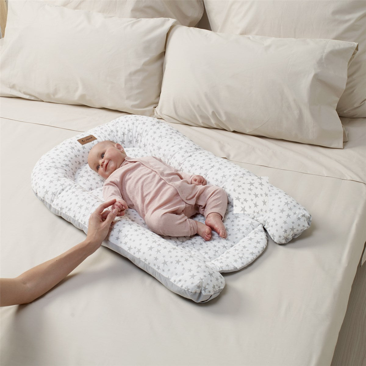 Baby lying on a white pillow with star patterns on a beige bed.