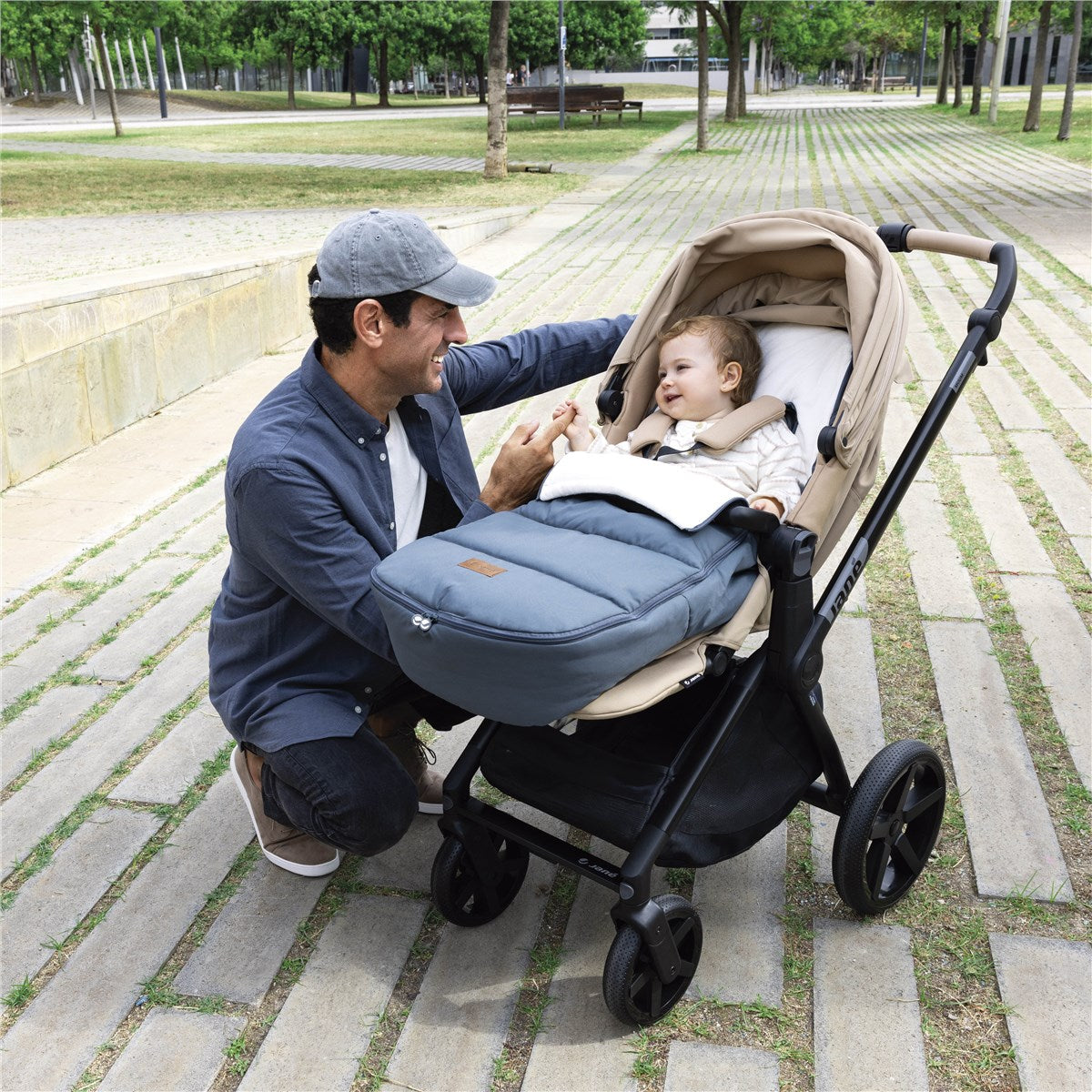 Man adjusting a baby in a stroller on a park path
