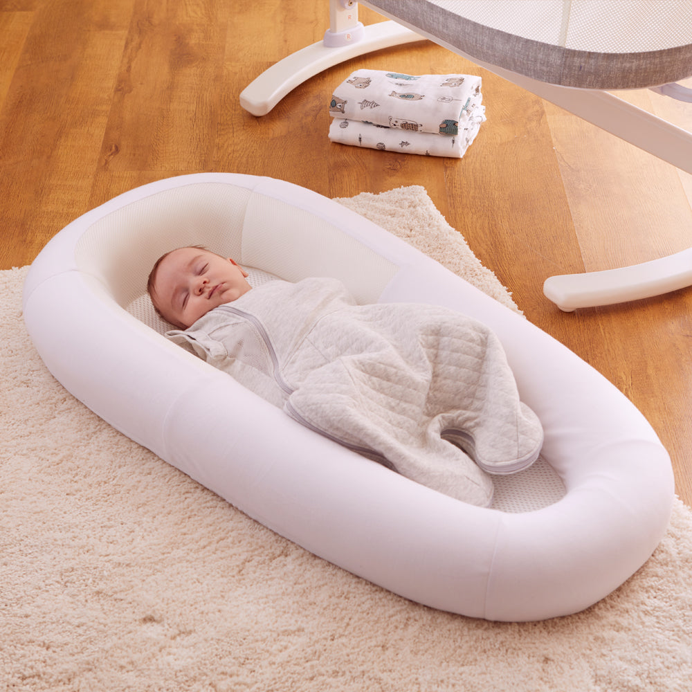 Baby sleeping in a white baby bed on a wooden floor.