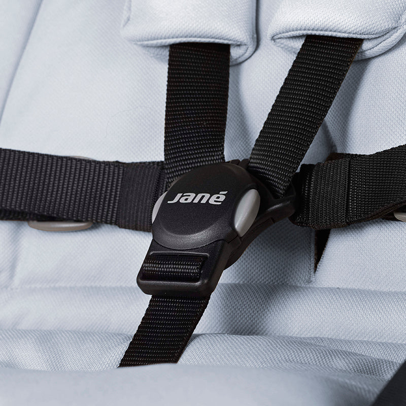 Close-up of a stroller seat with black straps featuring the 'jané' brand logo.