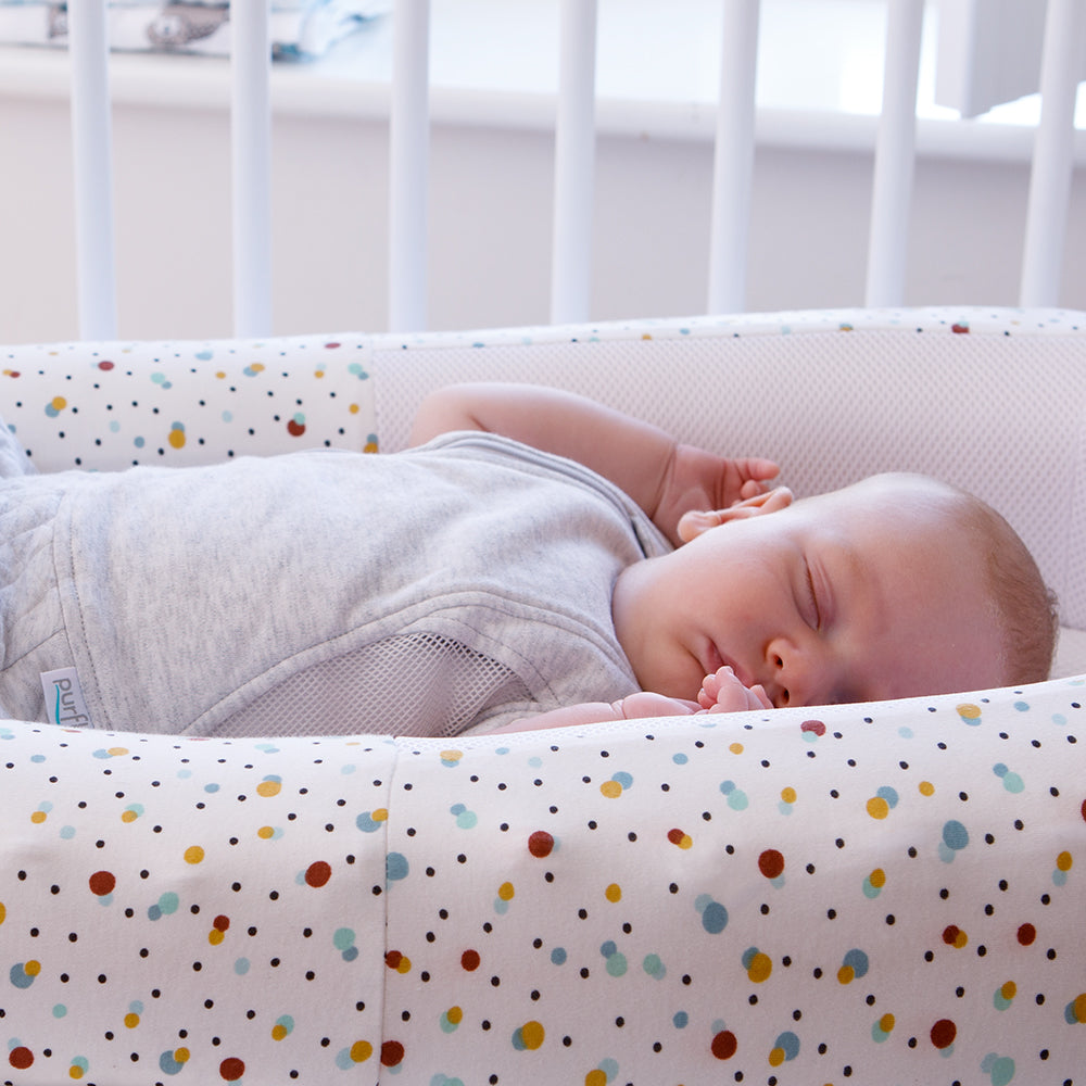 Baby sleeping in a crib with colorful polka dot bed.