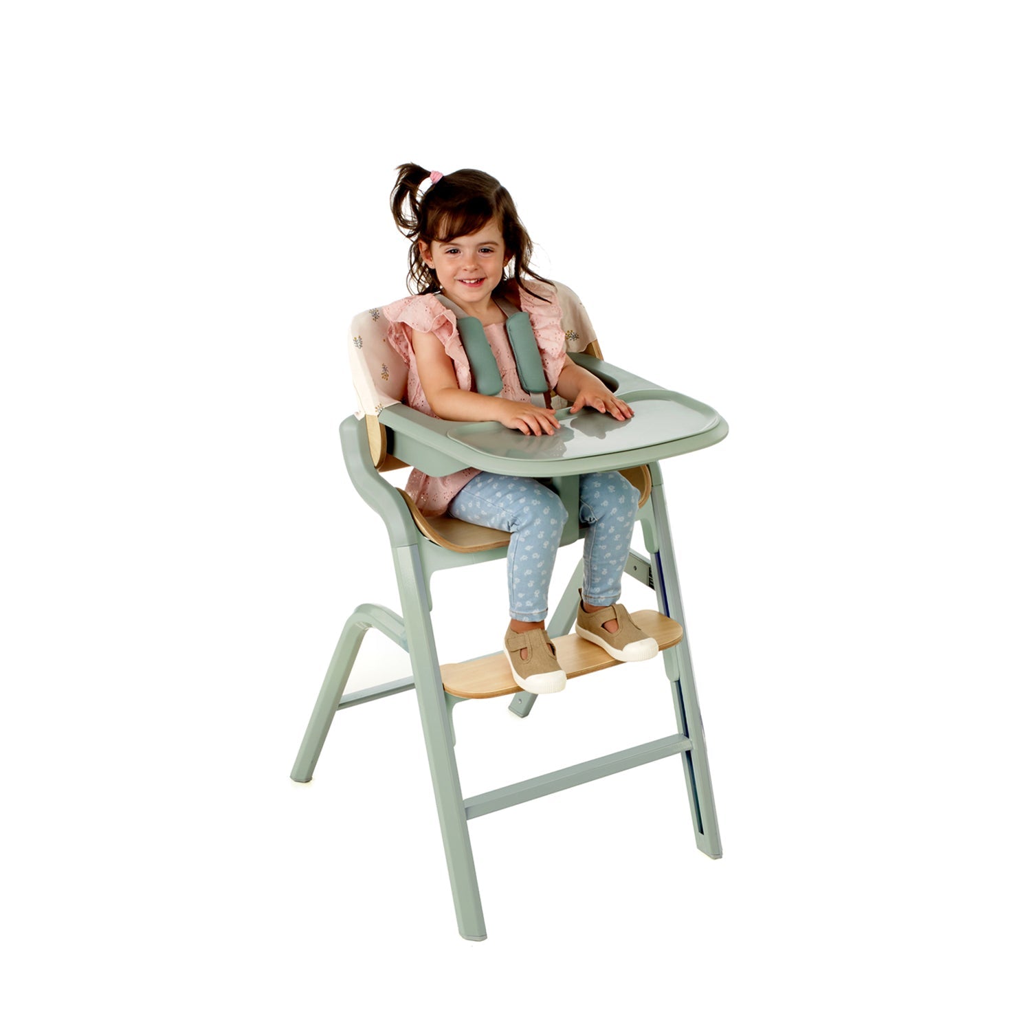 Child sitting in a green high chair with a white background