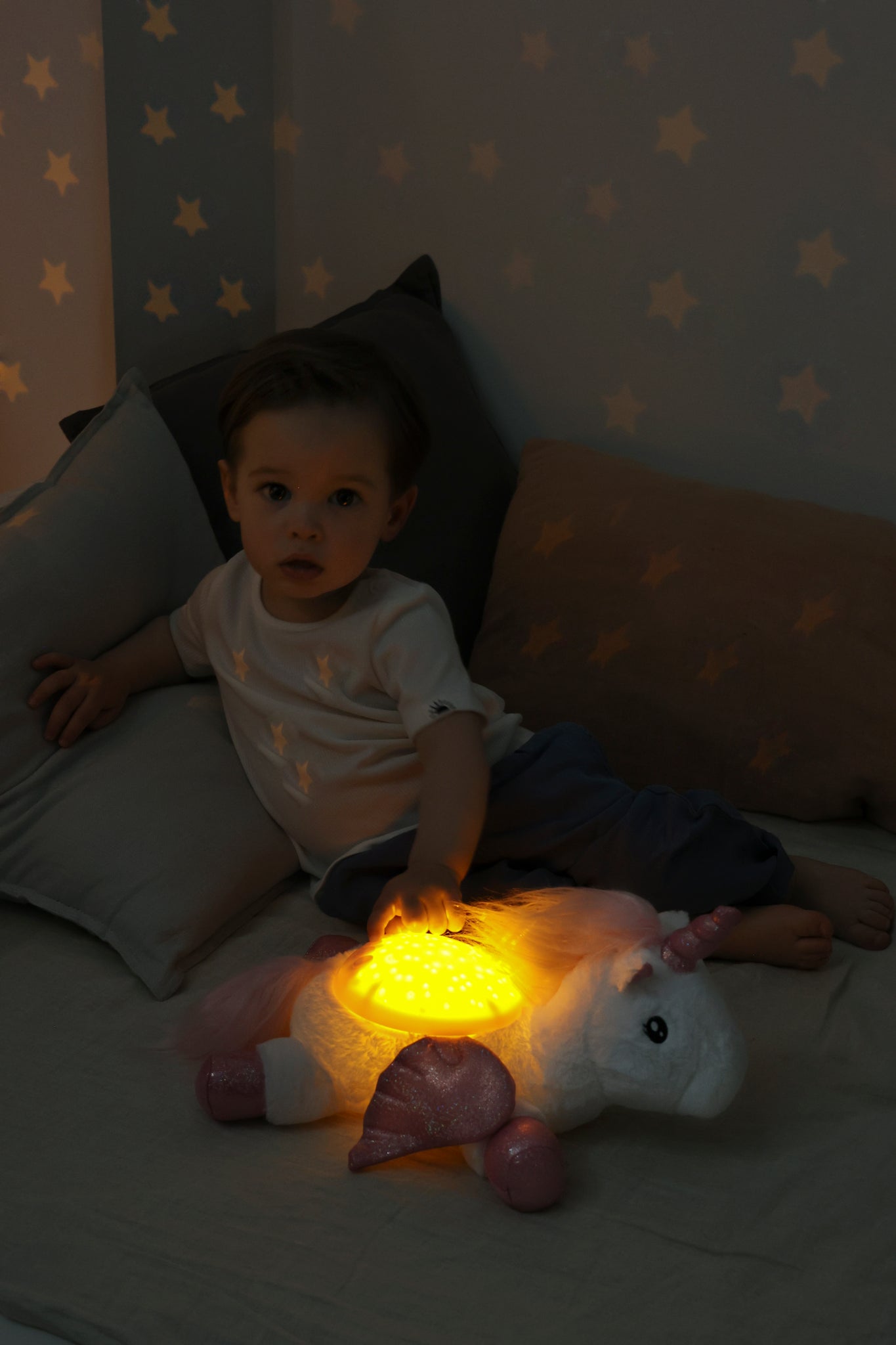 Child sitting on a bed with a glowing plush toy, surrounded by star-lit walls.