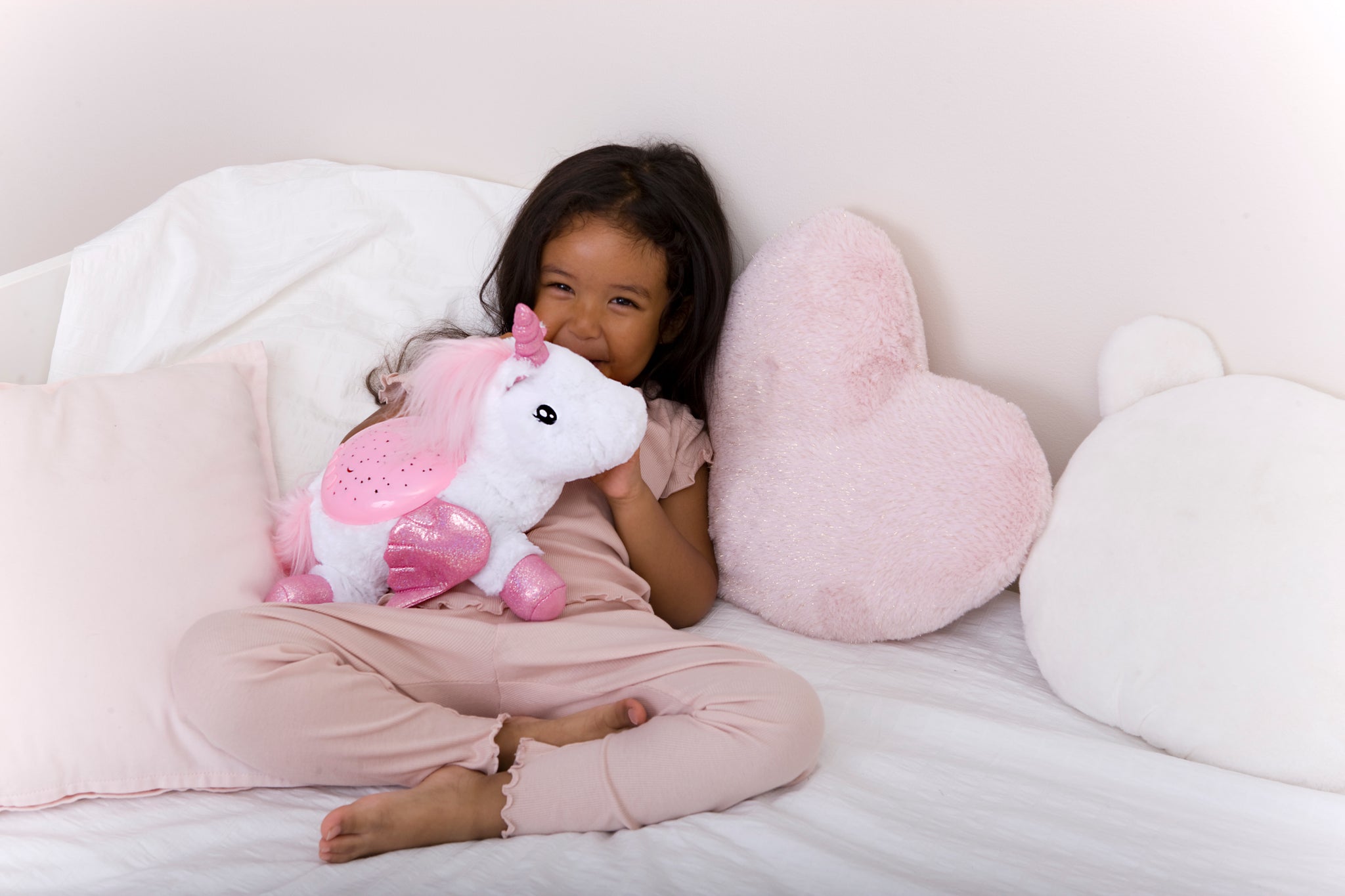 Child holding a pink unicorn plush toy on a white couch