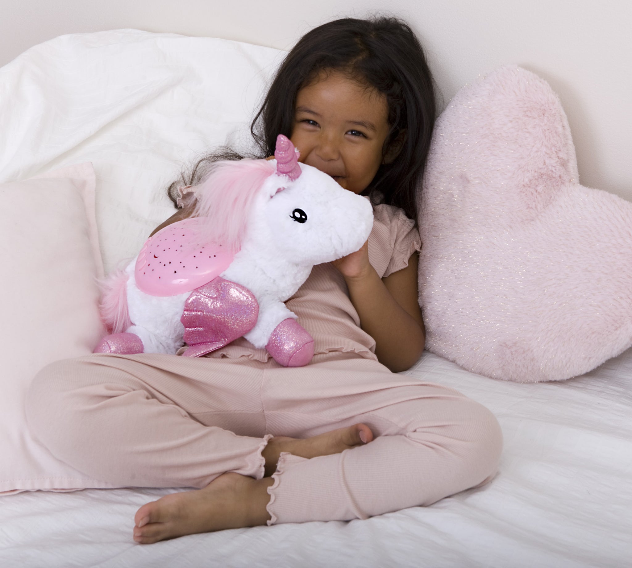 Child holding a pink and white unicorn plush toy on a bed