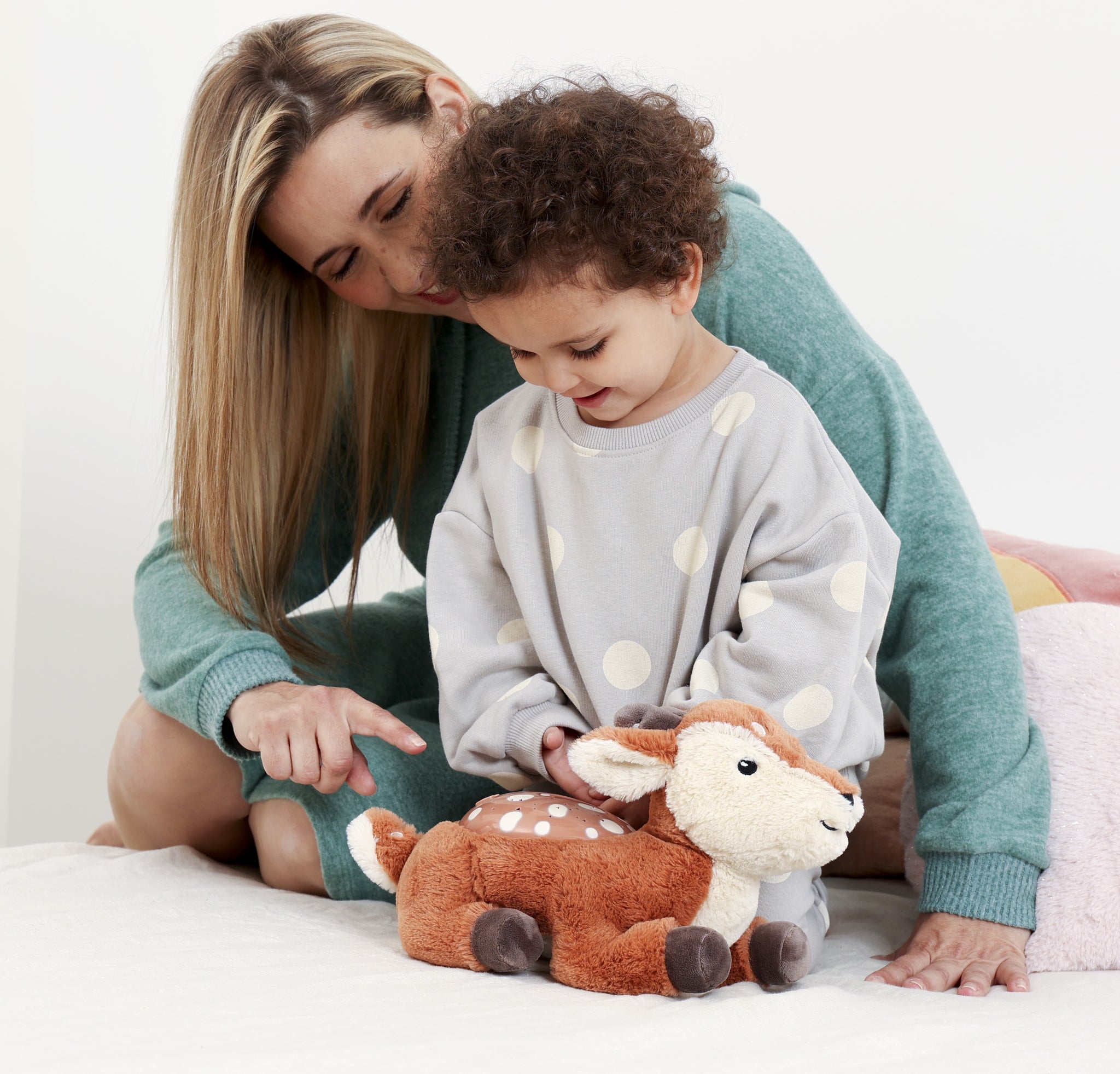 Woman and child playing with a plush deer toy on a bed