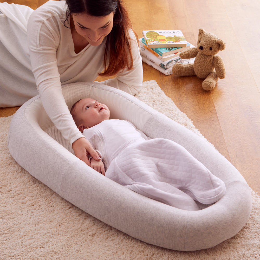 Woman with a baby in a white baby bed on a carpeted floor.