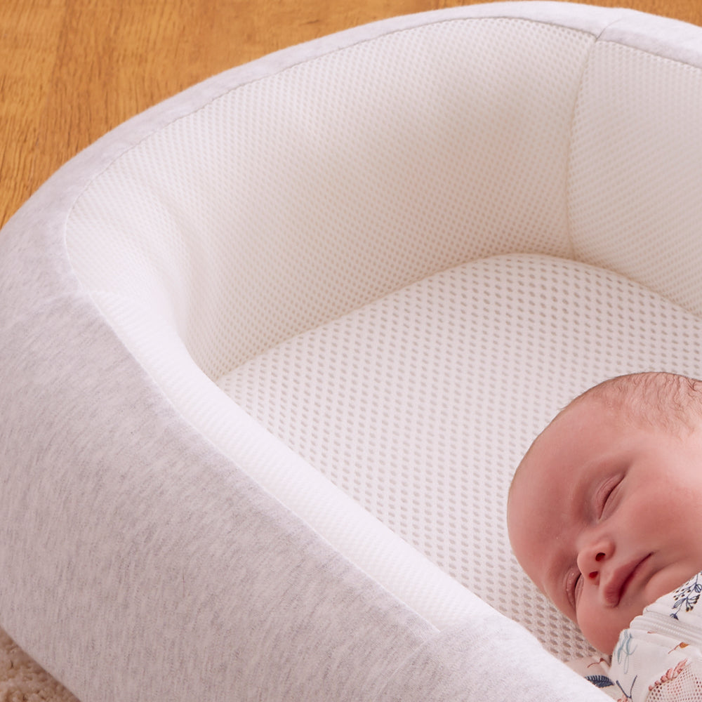 Newborn baby sleeping in a white and grey baby bed on a wooden floor.