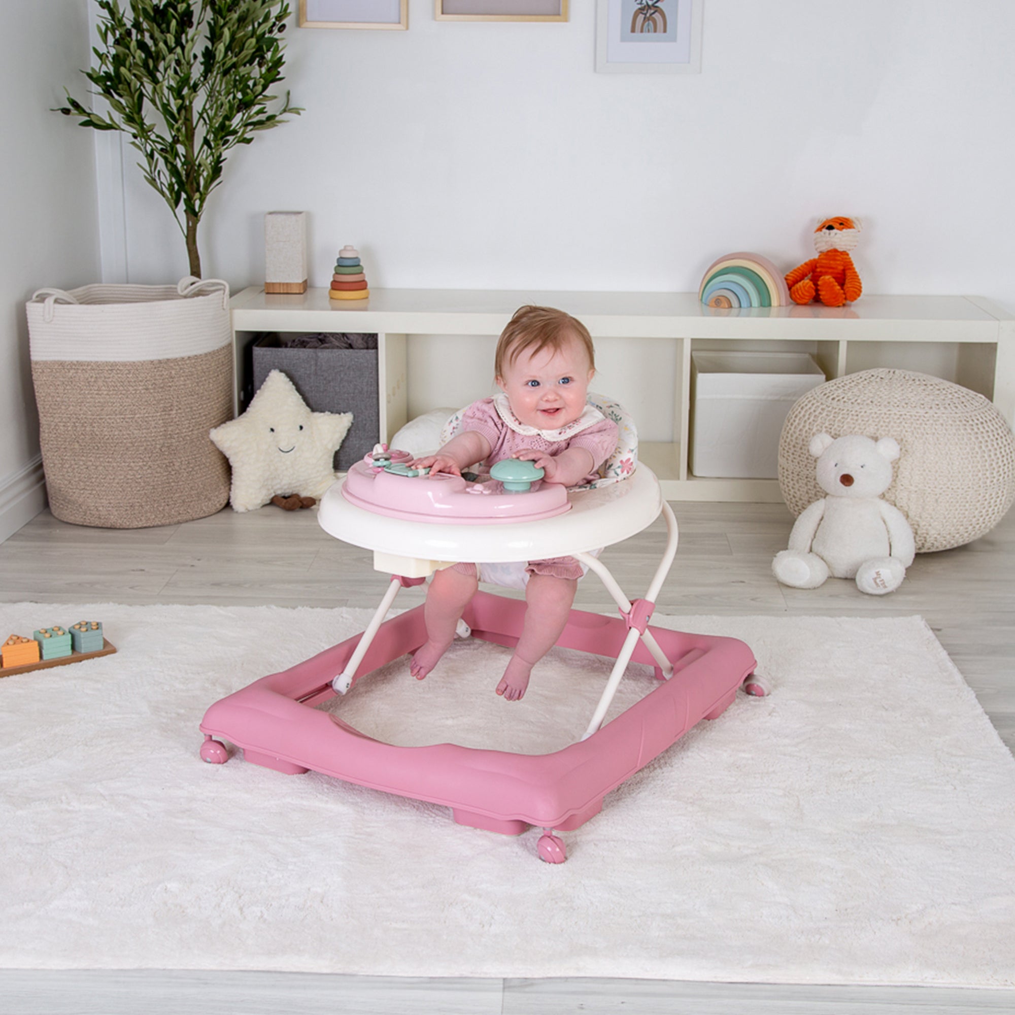 Baby in a pink and white walker in a room with toys and decor.