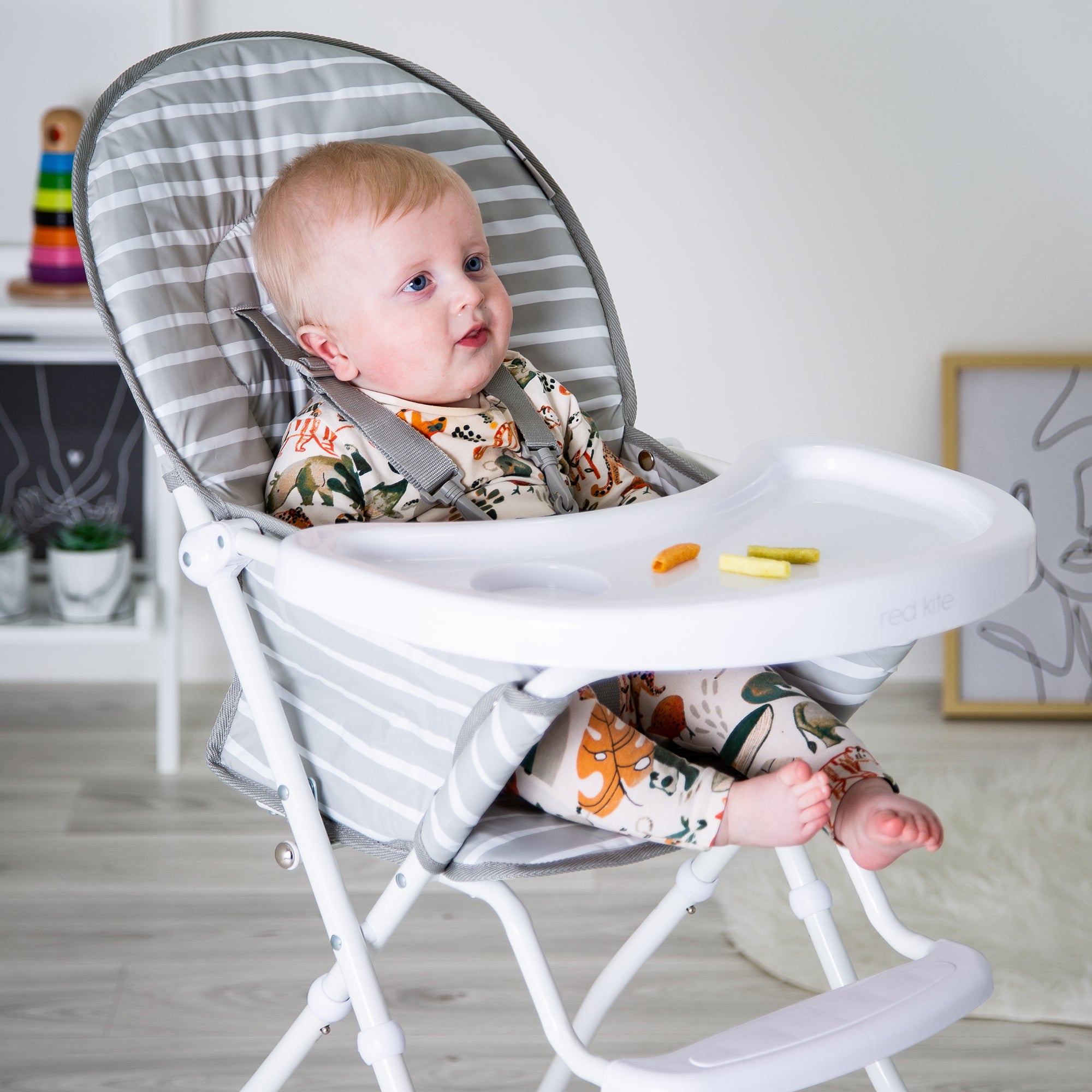 Baby sitting in a high chair with a tray in a room setting