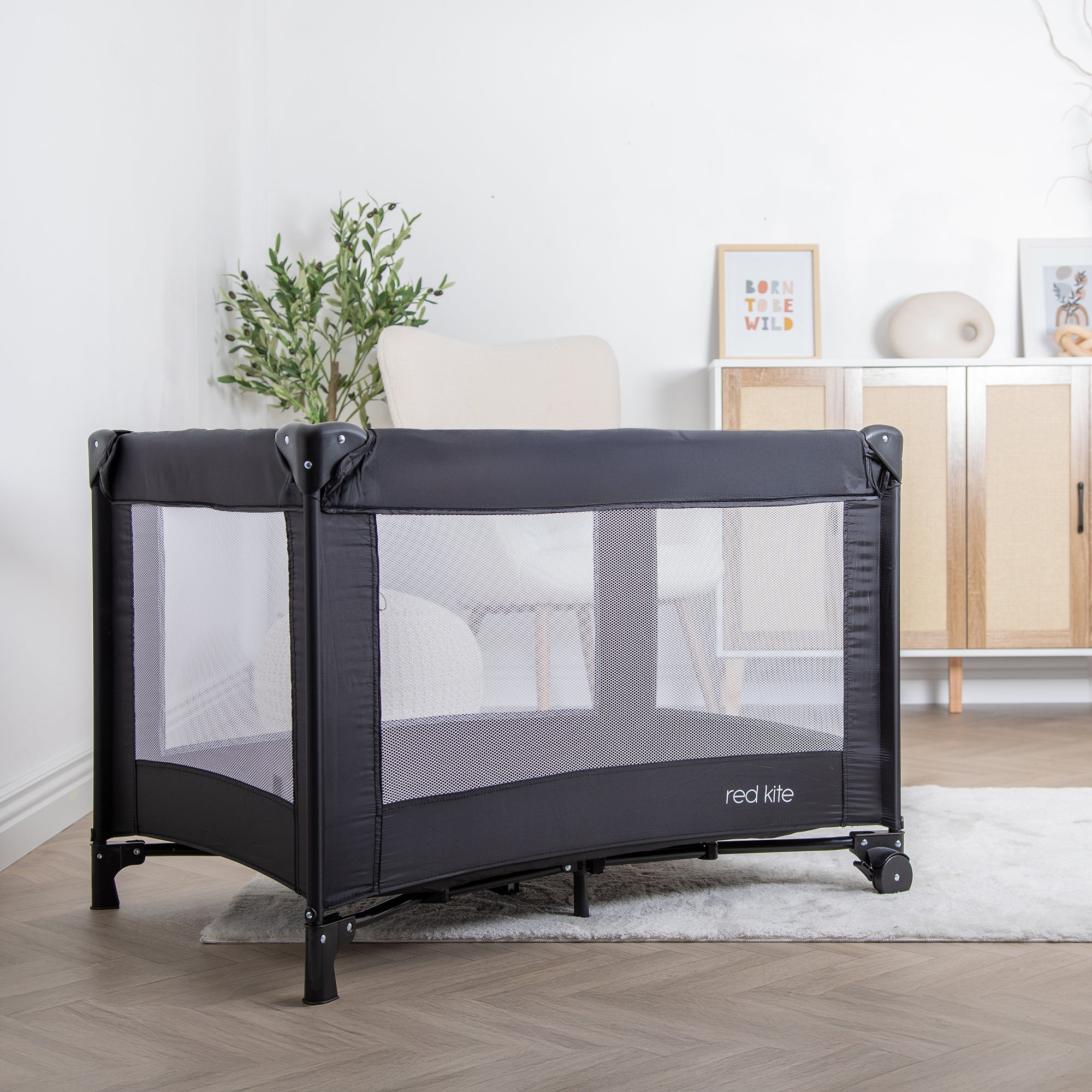 Black baby crib with mesh side on a wooden floor in a room setting