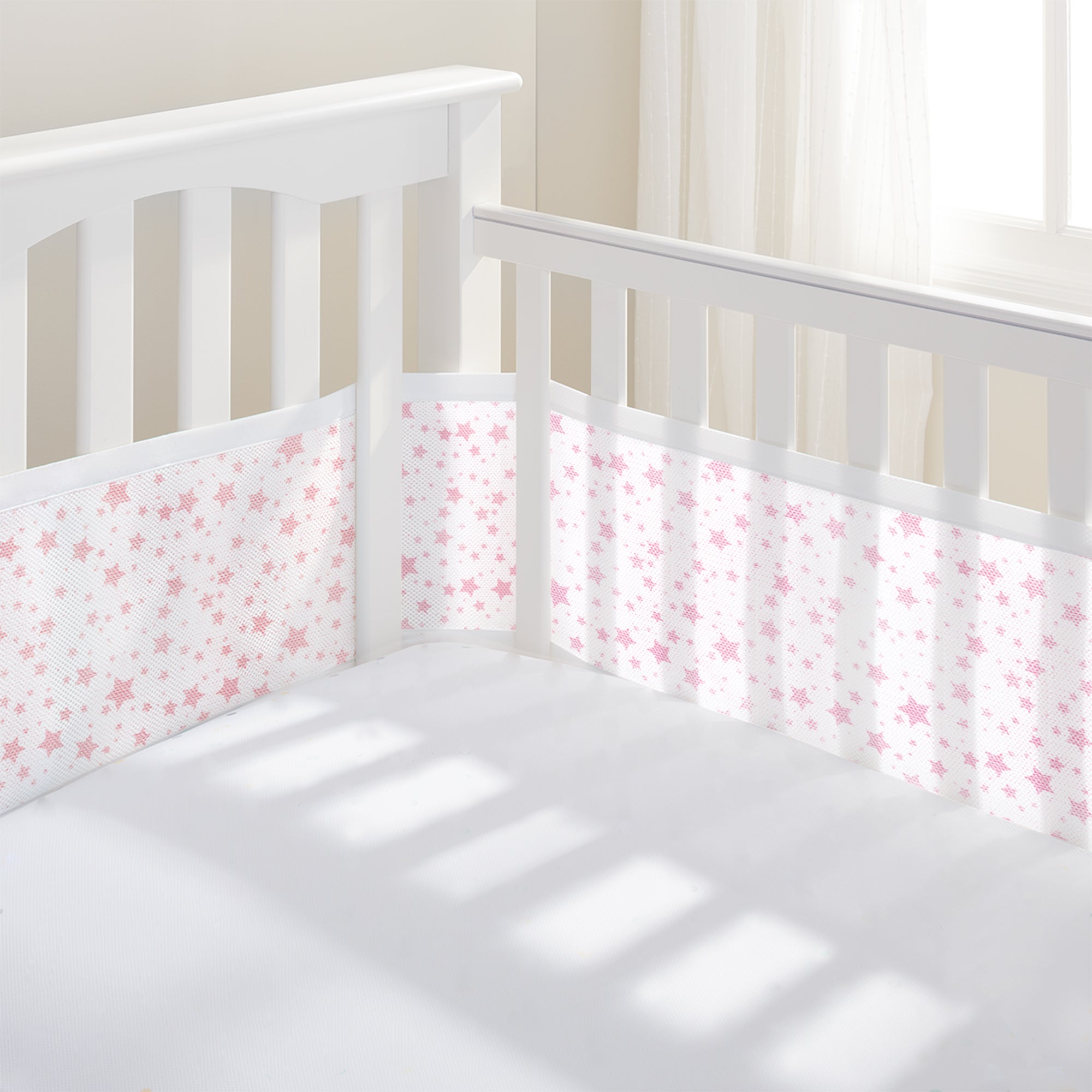 White crib with pink star-patterned bumper