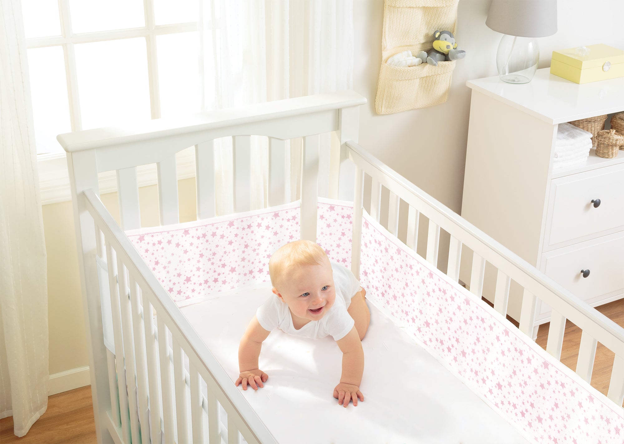 baby in cot with cot liner with pink stars on in nursery setting