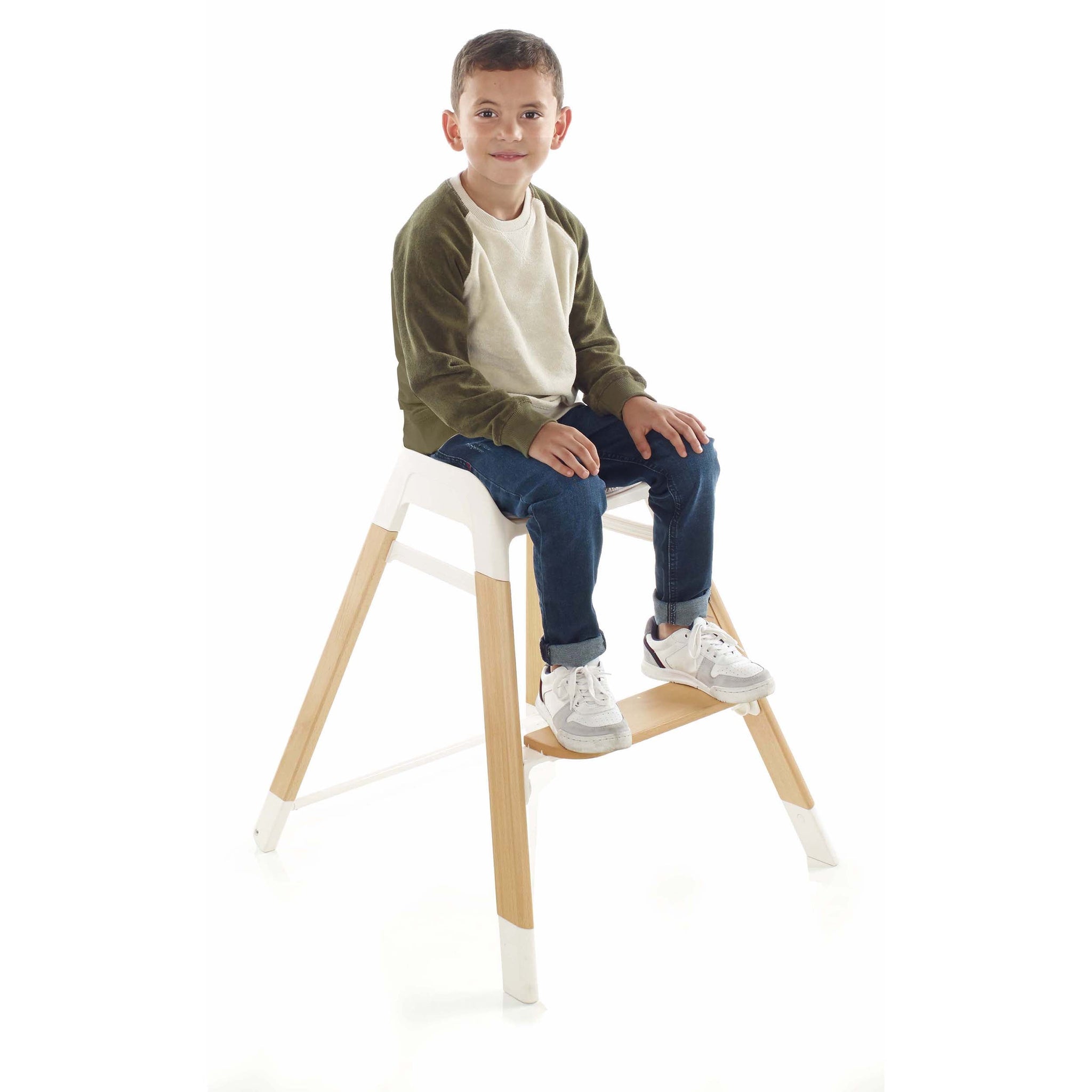 Child sitting on a white stool with wooden legs against a white background