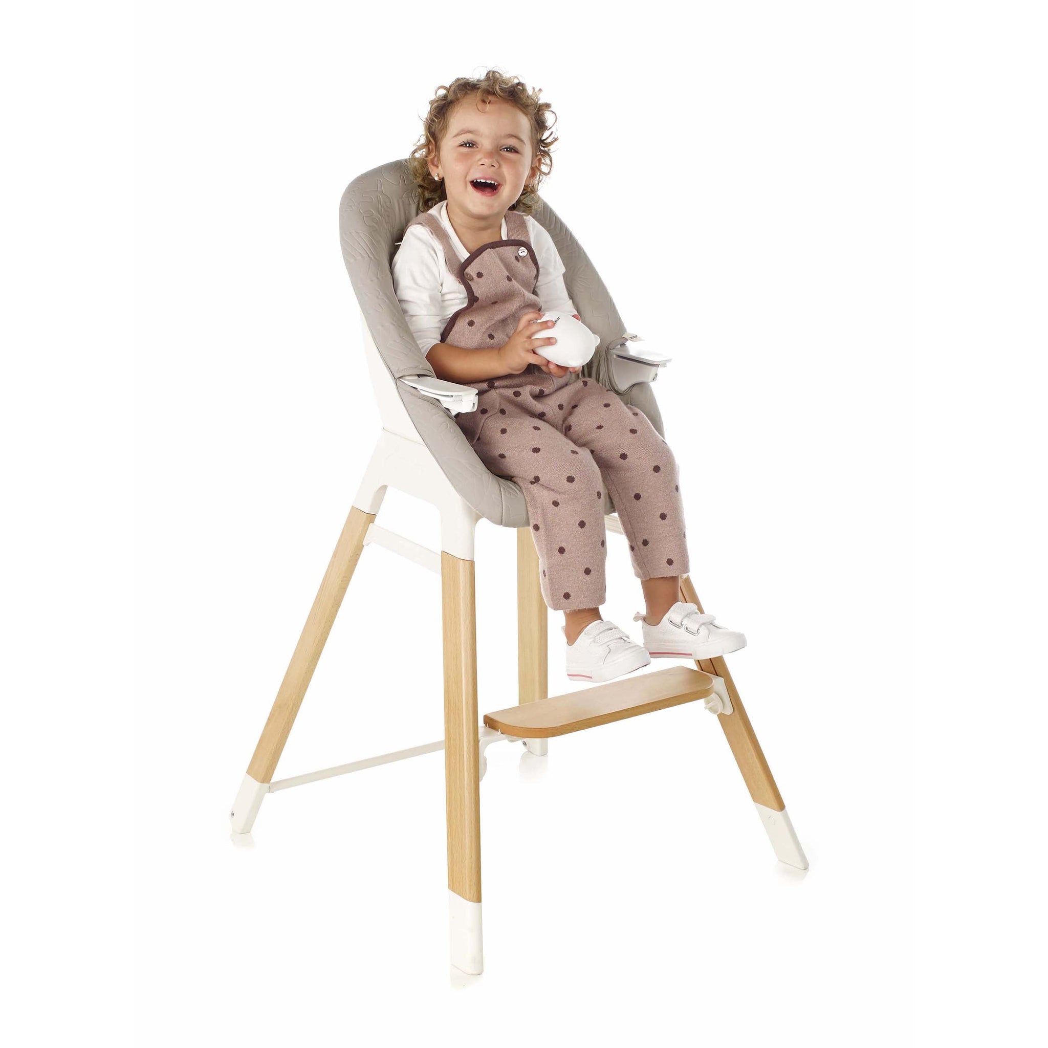 Child sitting on a high chair with beige cushion and wooden legs on a white background