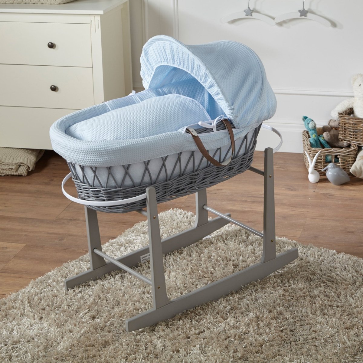 Baby Moses basket with blue cover on a stand in a nursery setting