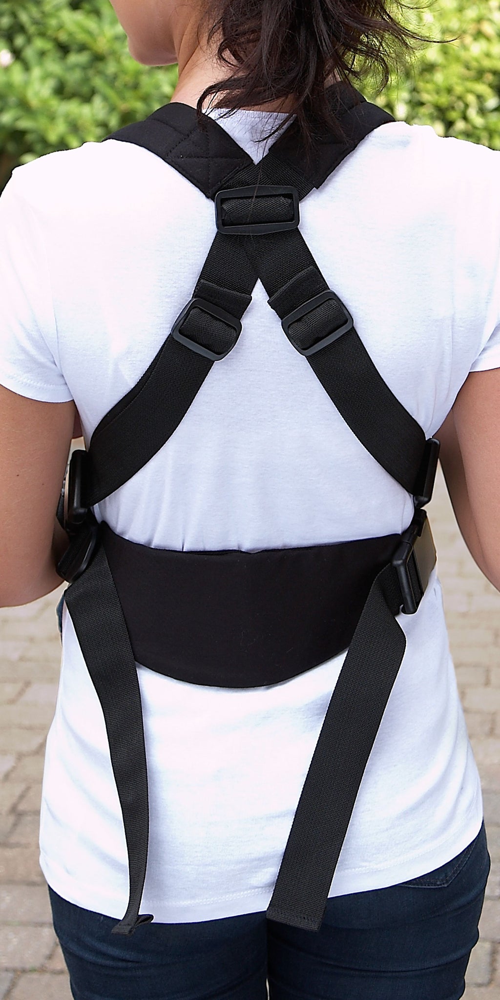 Person wearing a baby carrier from behind against a blurred outdoor background