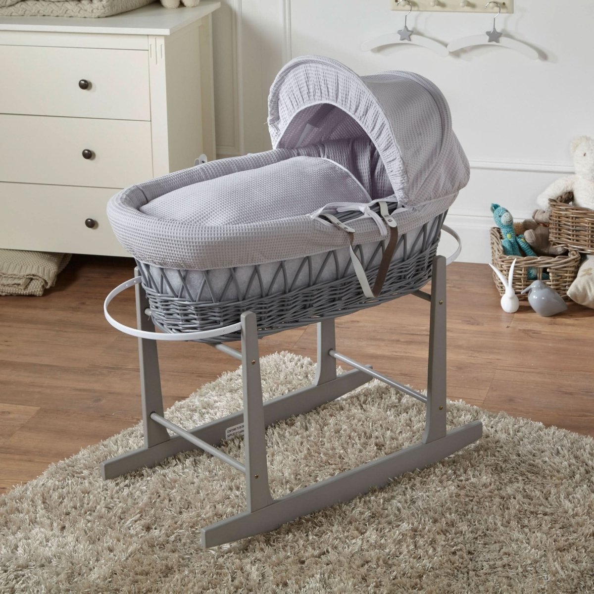 Gray wicker baby Moses basket on a stand in a nursery setting