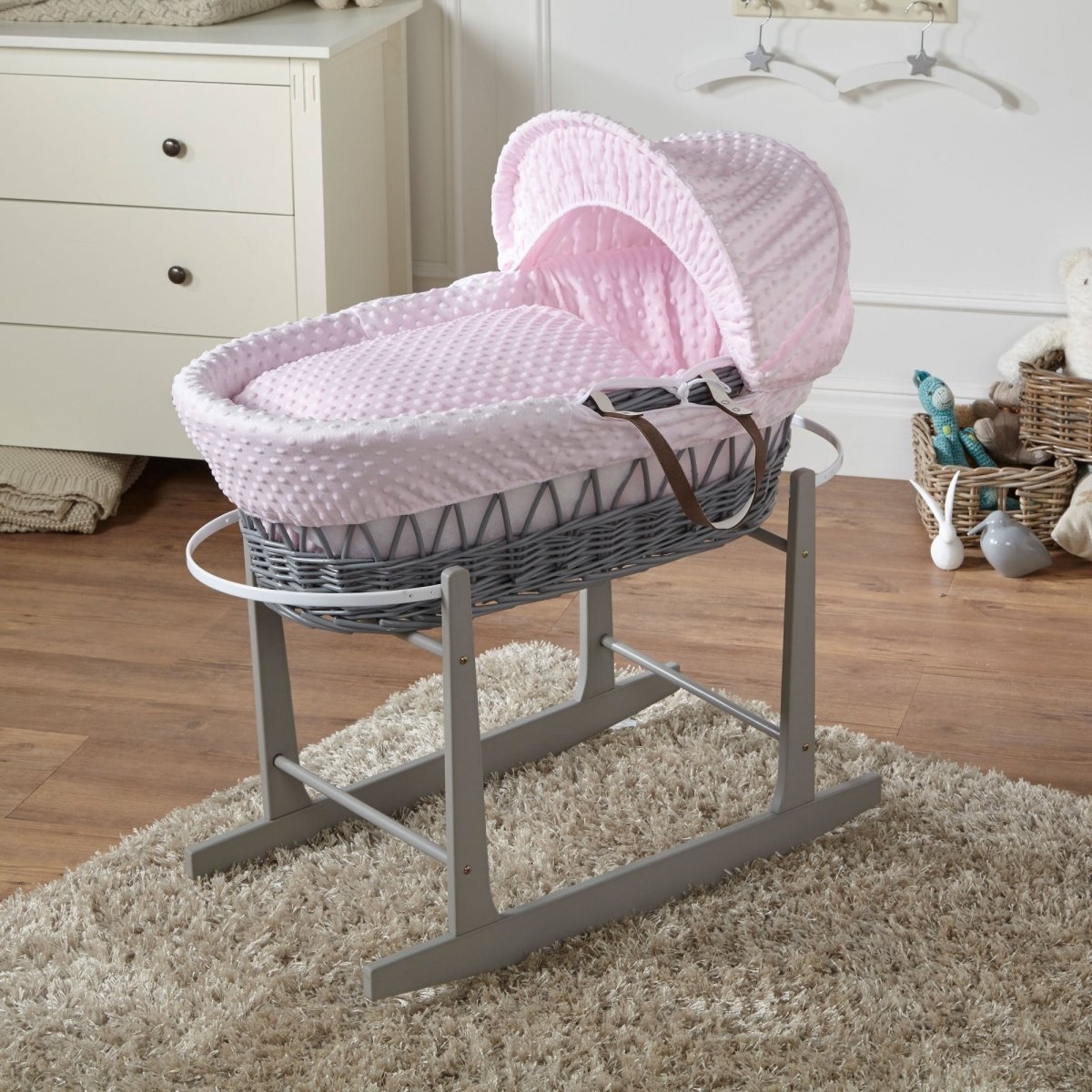 Pink wicker baby Moses basket on a stand in a nursery setting