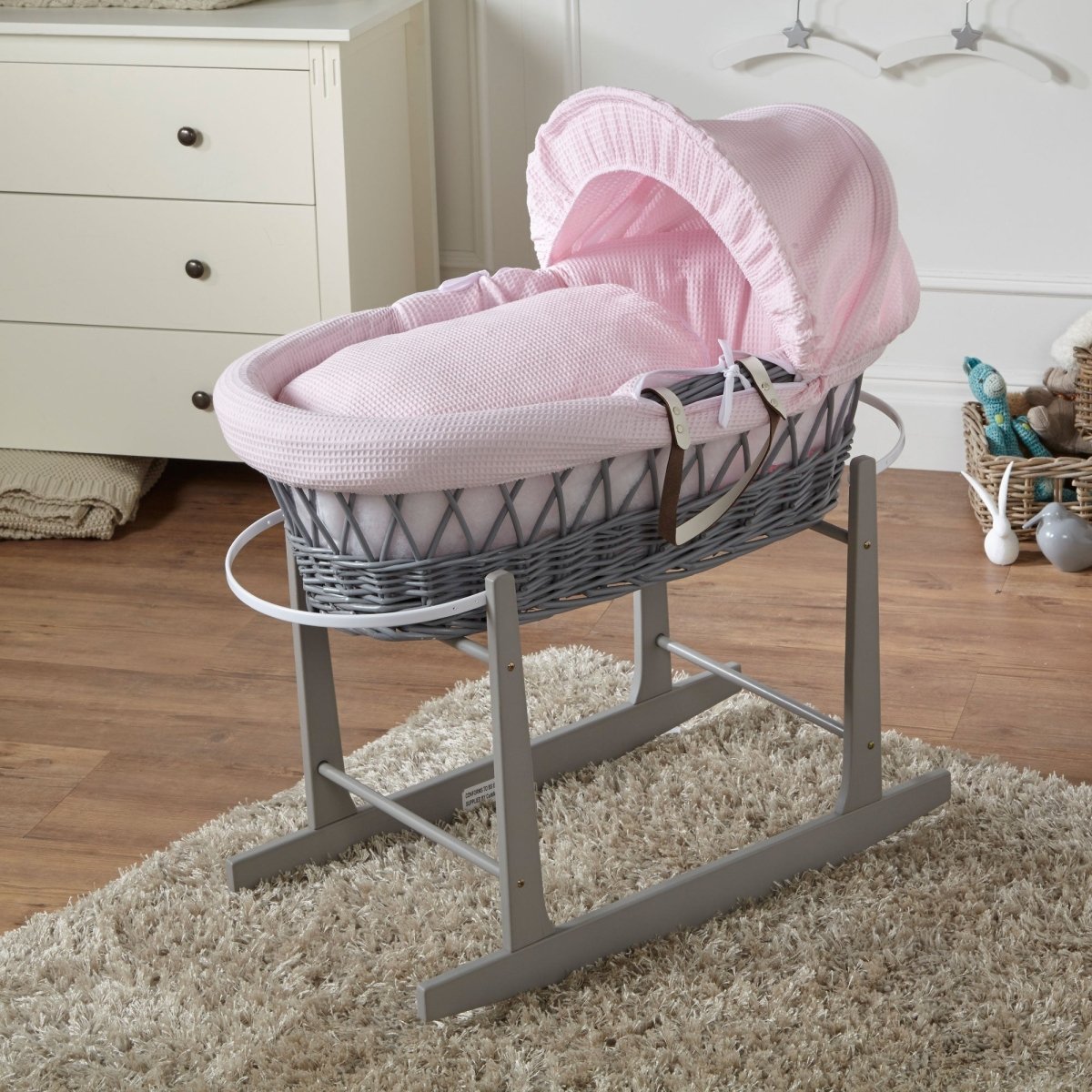 Gray Moses basket with pink cover on a stand in a nursery setting